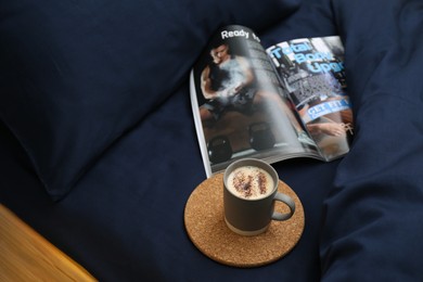 Open magazine and cup of coffee on bed with stylish silky linens, above view