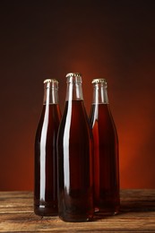 Photo of Bottles of delicious kvass on wooden table against brown background