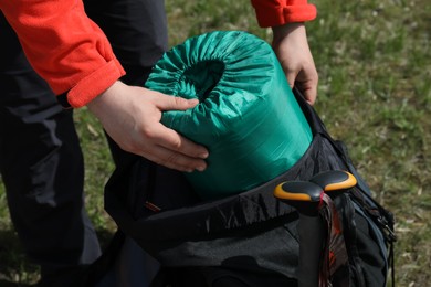 Hiker putting sleeping bag into backpack outdoors, closeup
