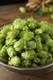 Photo of Fresh green hops in sieve on wooden table, closeup