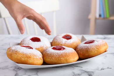 Woman taking Hanukkah doughnut with jelly and sugar powder at white marble table indoors, closeup