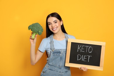 Happy woman holding broccoli and chalkboard with words Keto Diet on yellow background