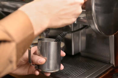Barista steaming milk using coffee machine, closeup