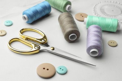 Sewing threads, scissors and buttons on white marble table