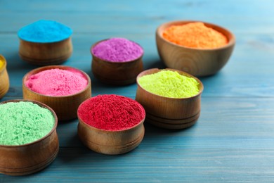 Colorful powder dyes on light blue wooden background, closeup. Holi festival