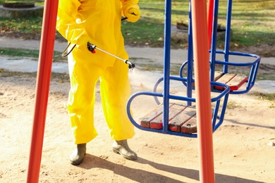 Person in hazmat suit with disinfectant sprayer cleaning children's playground, closeup. Surface treatment during coronavirus pandemic