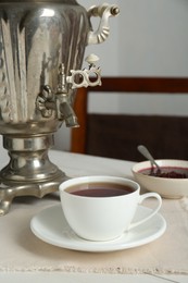Photo of Vintage samovar and cup of hot drink served on white wooden table. Traditional Russian tea ceremony