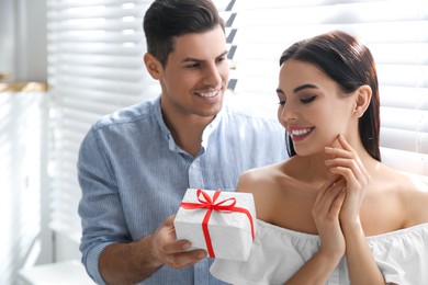 Man presenting gift to his beloved woman at home. Valentine's day celebration