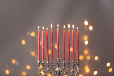 Silver menorah with burning candles against grey background and blurred festive lights. Hanukkah celebration