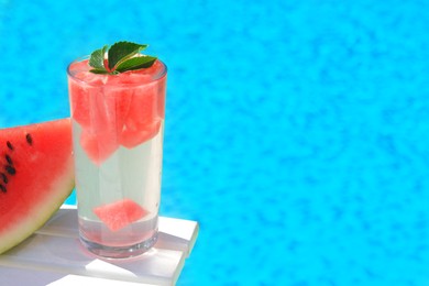 Refreshing watermelon drink in glass near swimming pool outdoors. Space for text