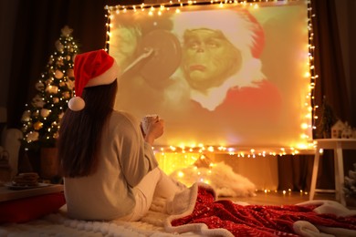 MYKOLAIV, UKRAINE - DECEMBER 24, 2020: Woman watching The Grinch movie via video projector in room. Cozy winter holidays atmosphere