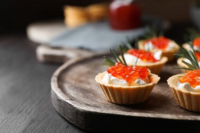 Photo of Delicious tartlets with red caviar and cream cheese served on wooden table, closeup. Space for text