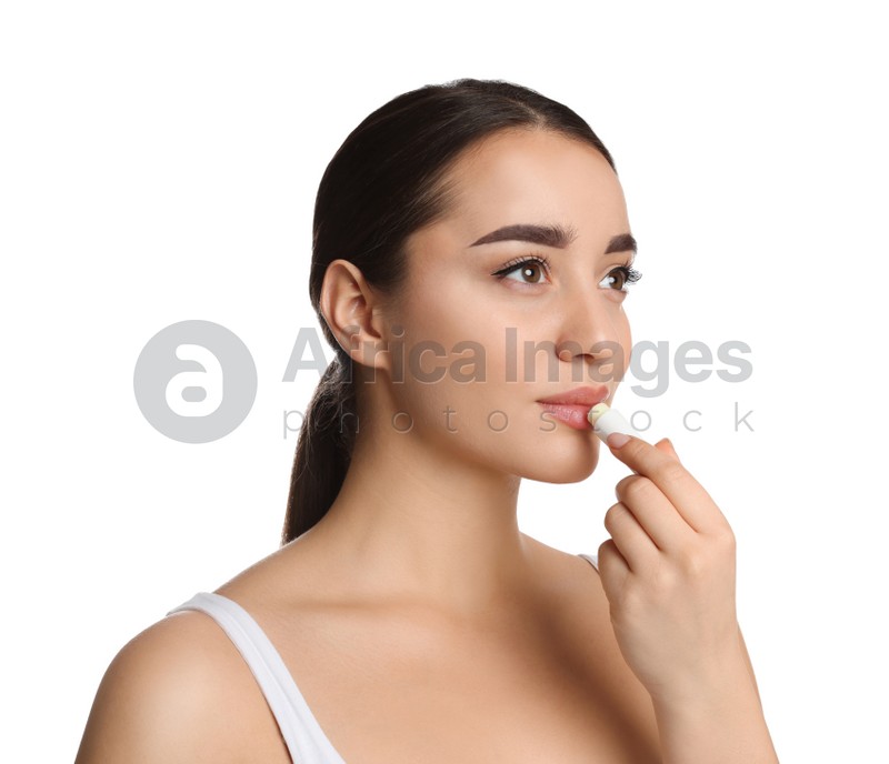 Young woman applying lip balm on white background