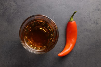 Red hot chili pepper and vodka in glass on grey table, flat lay