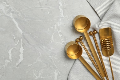 Golden cooking utensils and tablecloth on grey marble table, flat lay. Space for text