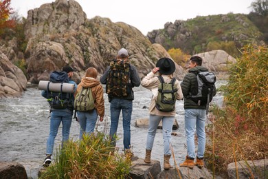 Photo of Group of friends with backpacks near mountain river on autumn day, back view