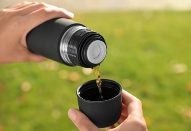 Woman pouring hot drink from thermos into cap outdoors, closeup