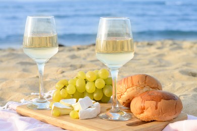 Photo of Glasses with white wine and snacks for beach picnic on sandy seashore