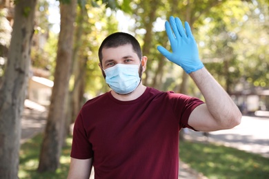 Man in protective face mask showing hello gesture outdoors. Keeping social distance during coronavirus pandemic
