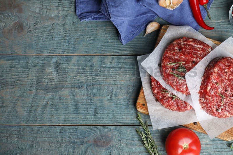 Flat lay composition with raw meat cutlets for burger on blue wooden table. Space for text