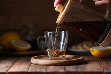 Woman pouring delicious tea into glass cup at wooden table, closeup