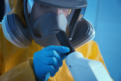 Scientist in chemical protective suit using microscope at laboratory, closeup. Virus research