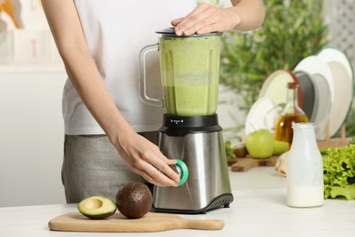 Woman preparing tasty green smoothie at white wooden table in kitchen, closeup