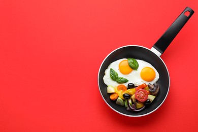 Tasty fried eggs with vegetables in pan on red background, top view. Space for text