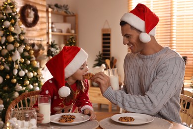 Photo of Happy father and his daughter eating delicious Christmas cookies at home