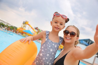 Mother and daughter taking selfie near pool in water park. Family vacation