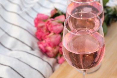Photo of Glasses of delicious rose wine and flowers on white picnic blanket, closeup