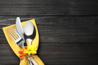 Top view of cutlery with napkin, autumn flower and ashberries on black wooden table, space for text. Thanksgiving Day
