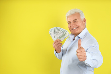 Happy senior man with cash money on yellow background. Space for text