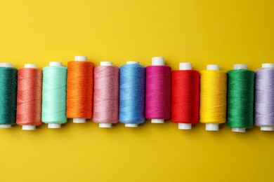 Set of colorful sewing threads on yellow background, flat lay