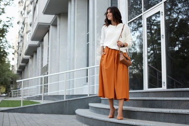 Young woman with stylish brown bag on stairs near building