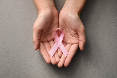 Woman holding pink ribbon on grey background, top view. Breast cancer awareness concept