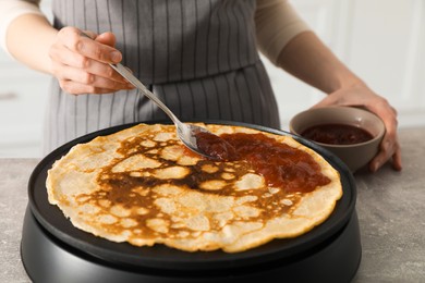 Photo of Woman cooking delicious crepe with jam on electric pancake maker in kitchen, closeup