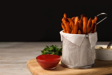Frying basket with sweet potato fries, sauces and parsley on table. Space for text