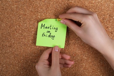 Photo of Woman pinning paper note with phrase Meeting On Friday to cork board, closeup