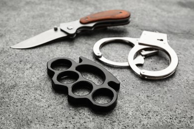 Brass knuckles, handcuffs and knife on grey background