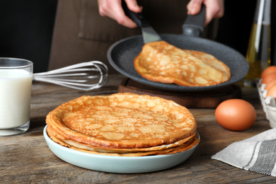 Woman cooking delicious thin pancakes at wooden table