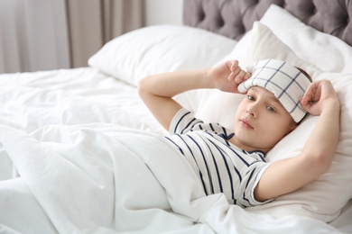 Little boy suffering from headache while lying in bed at home