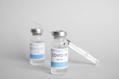 Vials with coronavirus vaccine and syringe on light background