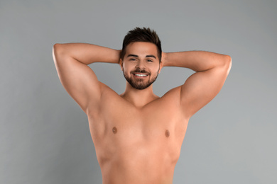 Young man showing hairless armpits after epilation procedure on grey background