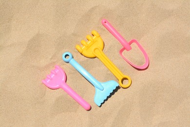 Photo of Bright plastic rakes and shovel on sand, flat lay. Beach toys