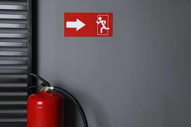 Fire extinguisher and emergency exit sign indoors. Space for text