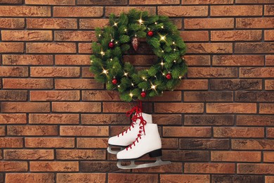 Pair of ice skates and beautiful Christmas wreath hanging on brick wall