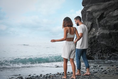 Young couple walking on beach near sea. Space for text
