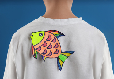 Preteen boy with paper fish on back against blue background,closeup. April fool's day