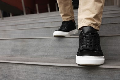 Photo of Man in stylish black leather sneakers walking down stairs, closeup. Space for text